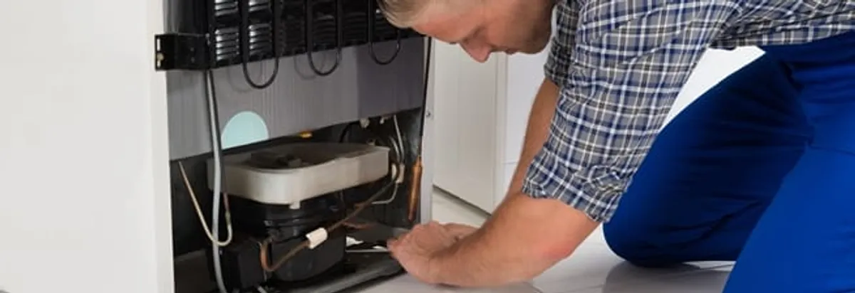 Refrigerator repair technician servicing the compressor and condenser area in Evansville, IN